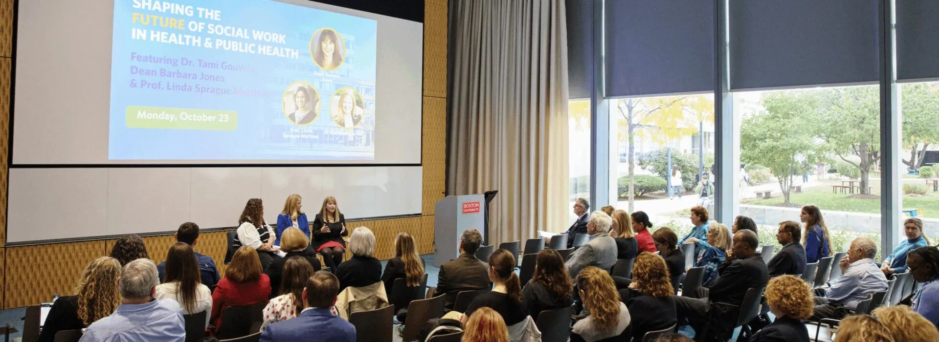 Audience members attend a CISWH event featuring Director Tami Gouveia and Dean Barbara Jones, with a panel discussion taking place at the front of the room beneath a large presentation screen.